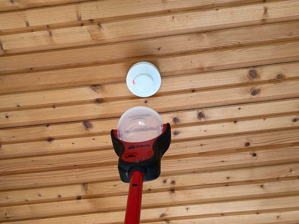 Prüfung eines Rauchwarnmelders an der Holzdecke mit Prüfstange